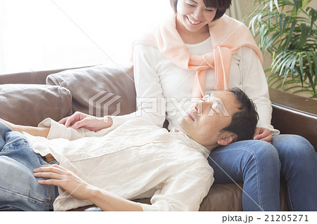 ひざまくらで眠る男性とソファに座る女性 21205271