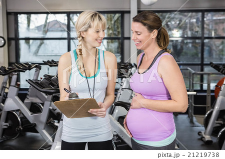 Smiling trainer showing clipboard to pregnant woman 21219738