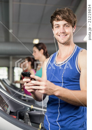 Smiling muscular man on treadmill listening to music Smiling muscular man on treadmill listening to music 21219834