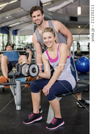 Trainer man helping woman lifting dumbbell Trainer man helping woman lifting dumbbell 21220211