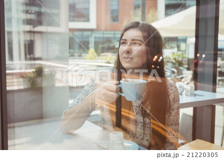 Woman looking through window with coffee Woman looking through window with coffee 21220305