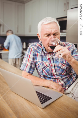 Senior man drinking red wine while using laptop 21220985