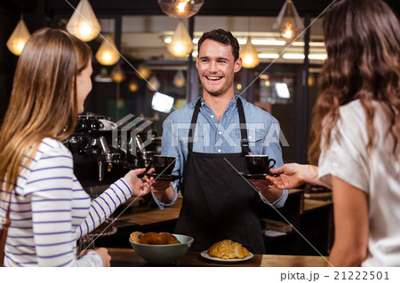 Smiling barista giving coffees to women 21222501