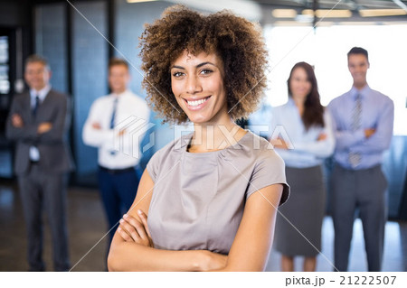 Businesswoman smiling at camera while her colleagues standing in Businesswoman smiling at camera while her colleagues standing in 21222507
