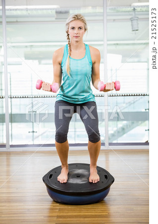 Fit blonde standing on bosu ball and lifting dumbbells 21525173