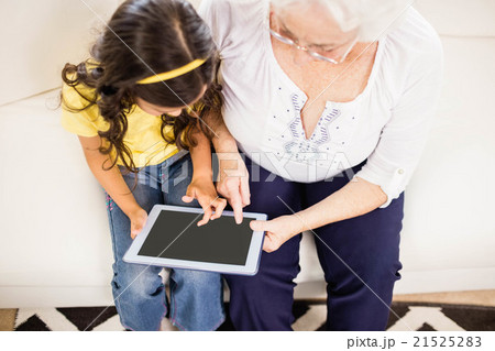 Concentrated granddaughter using tablet with grandmother 21525283