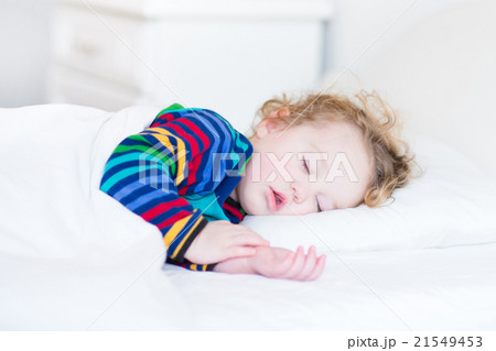 Adorable toddler girl taing a nap in white bedroom 21549453