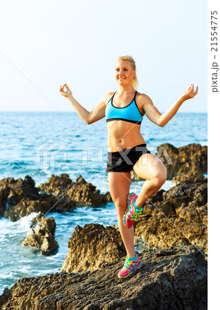 Happy athletic woman practicing yoga on the rocks by the sea 21554775