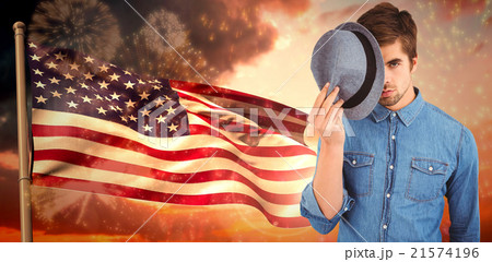 Composite image of portrait of hipster holding hat in front of f 21574196