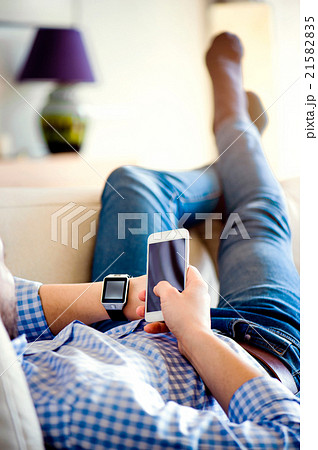 Man lying on sofa using smartphone and smart watch Man lying on sofa using smartphone and smart watch 21582835