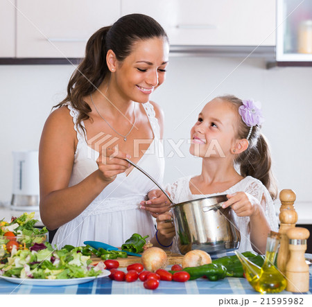 mother teaching daughter how to cook soup indoors 21595982