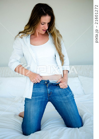 woman kneeling on her bed struggling to button her jeans woman kneeling on her bed struggling to button her jeans 21601272