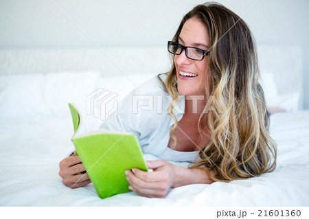 smiling woman lying on her bed reading smiling woman lying on her bed reading 21601360