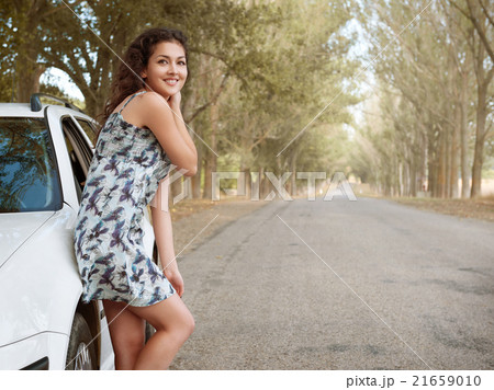 girl stand on country road near car, big high trees, summer season 21659010