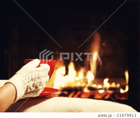 .Red cup of tea or coffee in hands near fireplace. 21679911