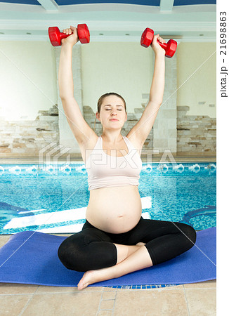 Pregnant woman sitting on mat near swimming pool Pregnant woman sitting on mat near swimming pool 21698863