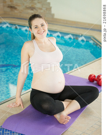 Happy pregnant woman posing on fitness mat at pool Happy pregnant woman posing on fitness mat at pool 21698868
