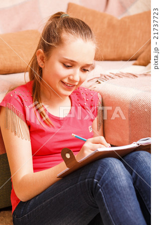 Young teenager girl writing in diary sits on floor Young teenager girl writing in diary sits on floor 21737723