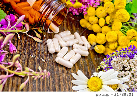 Capsules in brown jar with flowers on dark board 21789501