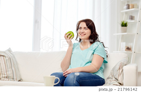 happy plus size woman eating green apple at home happy plus size woman eating green apple at home 21796142