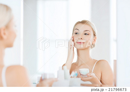 happy woman applying cream to face at bathroom happy woman applying cream to face at bathroom 21796673