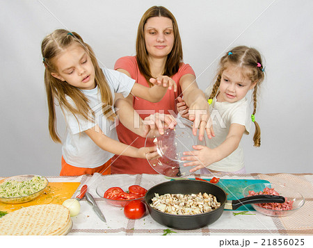 Mother with two daughters at the kitchen table with a plate of mushrooms is poured into the pan 21856025
