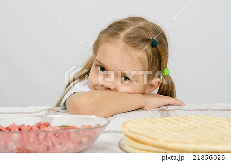 Little girl sitting at a table with his head on his hand with a smile and looking at the food 21856026