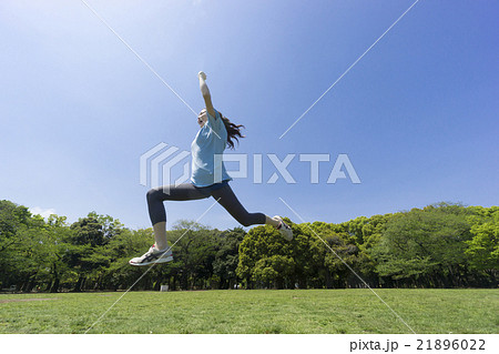 スポーツ 女性 公園でランニング ジャンプ快晴 青空 緑 横顔 気合いをいれて叫ぶ ガッツポーズの写真素材