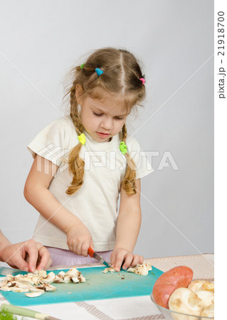 Little girl stands at the kitchen table and helps chop the mushrooms with a knife 21918700