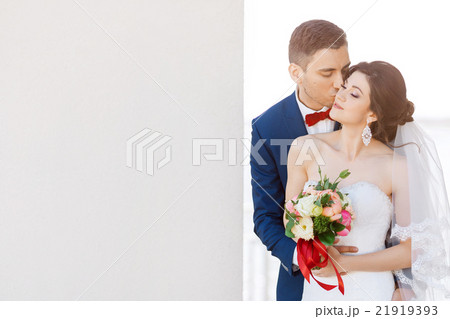 Young wedding couple kissing near a gray wall Young wedding couple kissing near a gray wall 21919393
