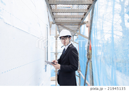 足場で建物の確認をするヘルメット姿の男性 21945135