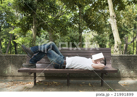 公園のベンチで昼寝をする男性の写真素材