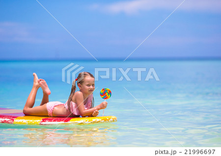 Little girl with lollipop have fun on surfboard in 21996697