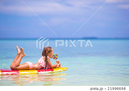 Little girl with lollipop have fun on surfboard in 21996698