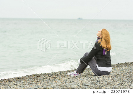 Young girl sitting on a pebble beach by the sea face to the sea breeze on a cloudy day Young girl sitting on a pebble beach by the sea face to the sea breeze on a cloudy day 22071978