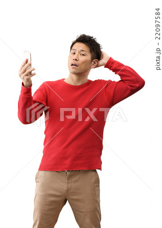 スマホを持って白バックに立っているカジュアルウェアーの30代男性のイメージ 22097584
