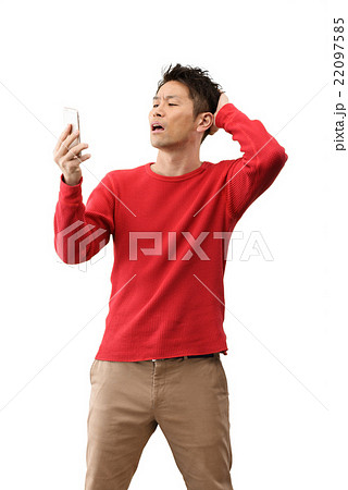 スマホを持って白バックに立っているカジュアルウェアーの30代男性のイメージ 22097585