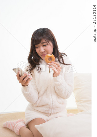 ドーナツを食べながらスマホを眺める女性 22130114