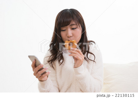 ドーナツを食べながらスマホを眺める女性 22130115