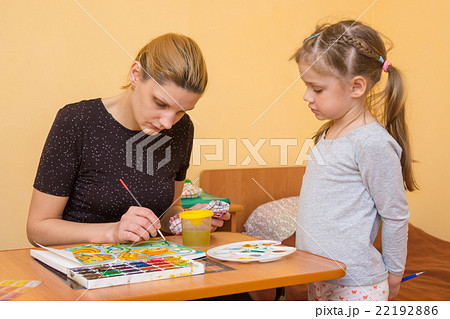 Little girl watches as the artist paints watercolors on paper at the table Little girl watches as the artist paints watercolors on paper at the table 22192886