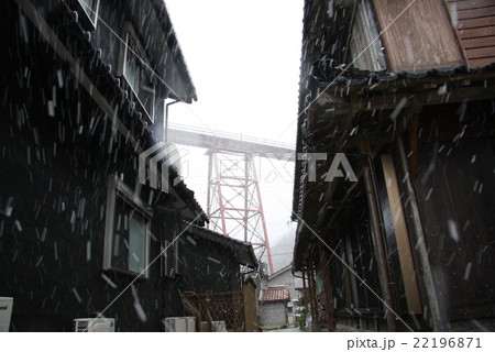 雪のなか民家をまたぐ旧式鉄橋を見上げる 22196871