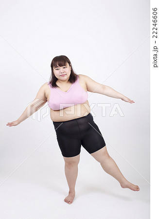 白い背景の前で片足立ちでバランスをとる太っている若い女性 22246606