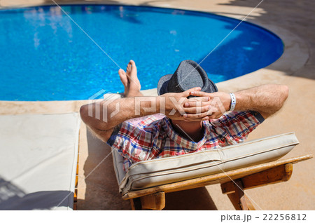 man in hat sunbathing on a sun lounger by the pool man in hat sunbathing on a sun lounger by the pool 22256812
