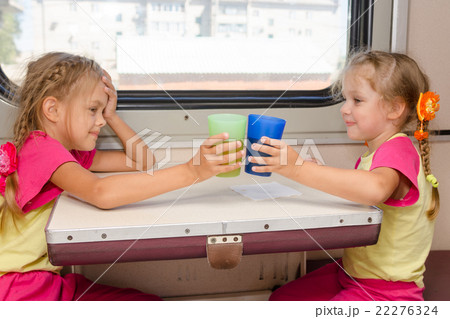 Two little sisters in identical pajamas drinking tea in the train at the table on outboard 22276324
