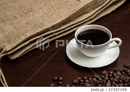 一杯のコーヒーカップとそれを挟むように置かれた麻袋とコーヒー豆　横から　クラシック 22302168
