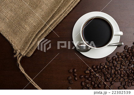 一杯のコーヒーカップとそれを挟むように置かれた麻袋とコーヒー豆　コピースペース多め　真俯瞰 22302539