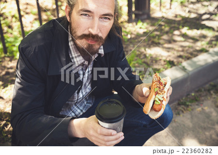 Asian man with hot dog and coffee in park Asian man with hot dog and coffee in park 22360282