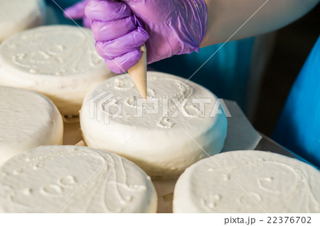 Worker's hand decorates white cake. 22376702