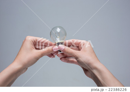 Hands holding an incandescent light bulb on gray Hands holding an incandescent light bulb on gray 22386226