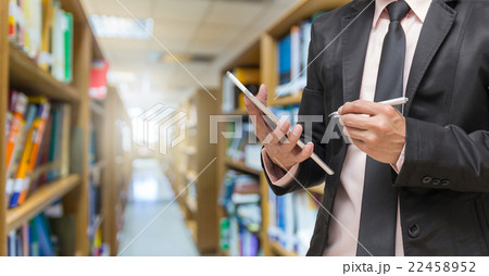 Businessman using the tablet on the Abstract blurred photo of library background Businessman using the tablet on the Abstract blurred photo of library background 22458952